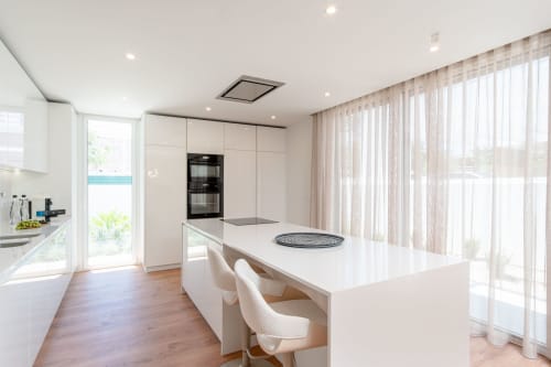 Modern kitchen island with white cabinetry, pool view access, and dining area in Villa Prestige Quinta do Pinhao II, Charneca