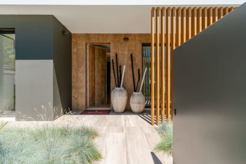 Modern villa entrance at Republica do Sul with wooden slats, decorative urns, and manicured garden in Aroeira