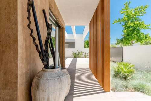 Modern villa corridor with striped flooring, wooden elements, and white pottery sculpture overlooking courtyard garden at