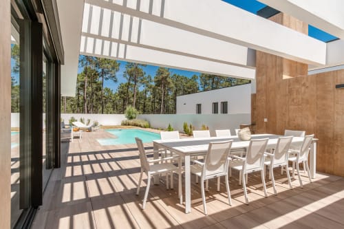 Modern villa terrace with dining area, lounge chairs, and turquoise pool overlooking pine forest in Aroeira, Portugal