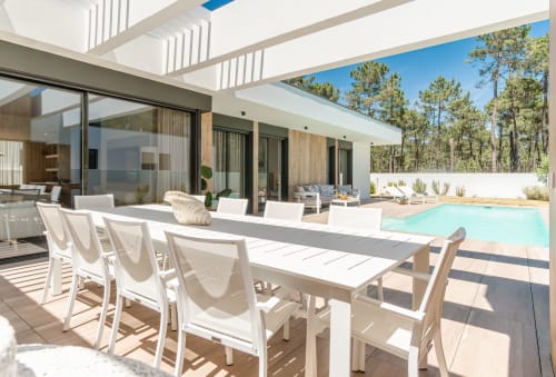 Modern villa terrace with dining table, lounge chairs, and swimming pool overlooking pine forest at Republica do Sul, Aroeira