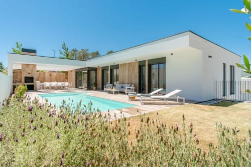 Modern villa with pool and lounge area in Aroeira, Portugal. White building with wooden accents, turquoise swimming pool, sun