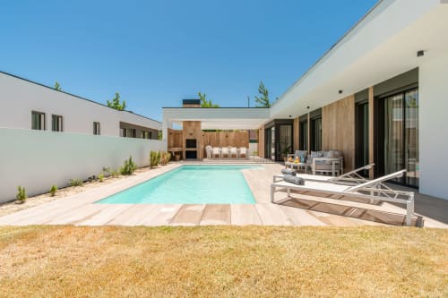 Modern villa with turquoise pool, wooden deck, lounge chairs, and white terrace building in Aroeira, Portugal