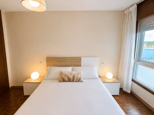 Moderno dormitorio del hotel Holibai en Baiona con vistas al océano, ropa de cama blanca y decoración costera