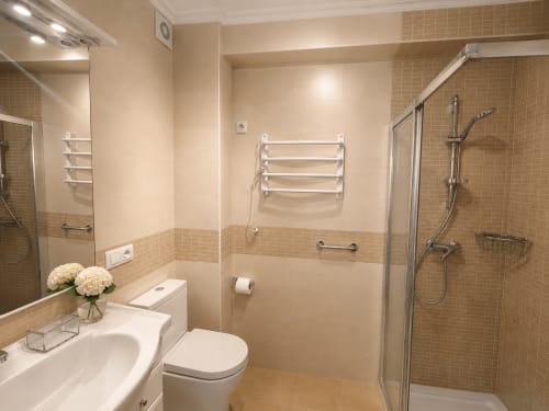 Baño moderno del hotel Holibai en Baiona con ducha, lavabo, inodoro, toallero térmico y paredes de azulejos beige