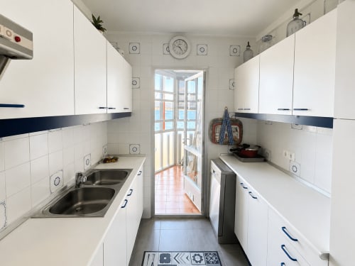Cocina de galera en Holibai, Baiona, con muebles blancos, doble lavabo y acceso a balcón