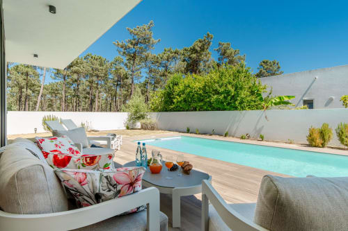 Área de estar de luxo à beira da piscina na Republica do Sul com piscina azul-turquesa, móveis modernos e cenário de floresta de pinheiros.