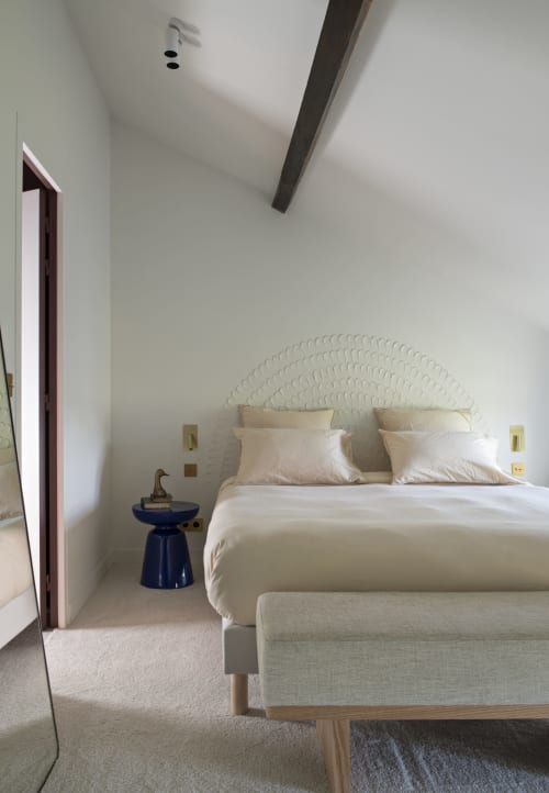 Chambre minimaliste au domaine by A&G avec tête de lit blanche texturée, linge crème, poutre bois foncé et table de nuit bleue