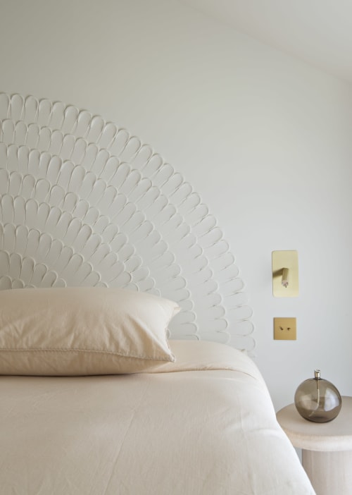 Chambre minimaliste au domaine by A&G avec tête de lit blanche décorée, literie crème, interrupteurs en laiton et lampe de chevet