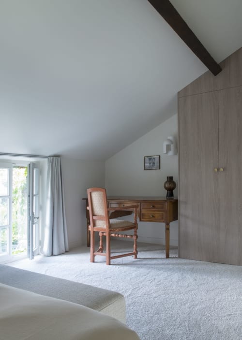 Chambre mansardée lumineuse au Domaine by A&G avec bureau en bois, chaise corail et vue sur le jardin par portes-fenêtres