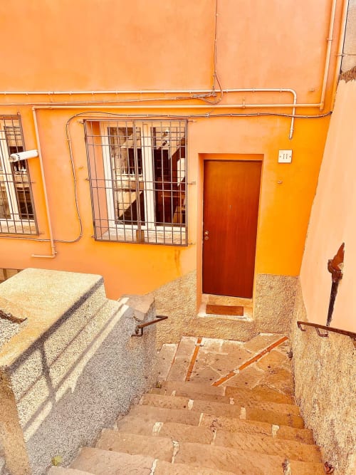 Ingresso dell'appartamento B&B Fossatello a Genova con facciata arancione, finestra blindata, porta rossa e gradini in piastrelle