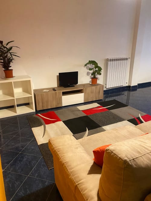 Elegante soggiorno del B&B Fossatello a Genova con TV, comode sedute, tappeto geometrico e piante in vaso