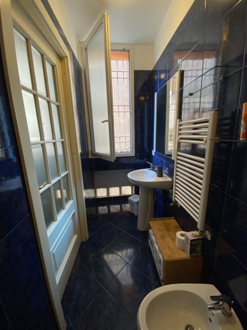 Bagno moderno con rivestimenti in piastrelle scure, lavabo a colonna, scaldasalviette e finestra al B&B Fossatello di Genova