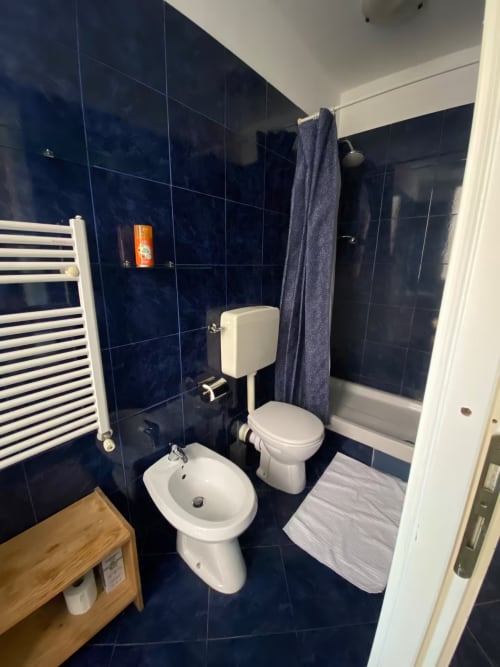 Bagno moderno con piastrelle blu scuro, sanitari bianchi e portasciugamani nell'appartamento di Genova