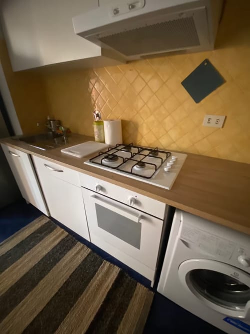 Cucina moderna dell'appartamento di Genova con fornello a gas, forno, mobili bianchi, rivestimento di piastrelle gialle e lavatrice