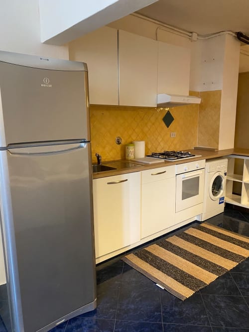 Cucina color crema con rivestimento giallo, frigorifero in acciaio inox, fornello a gas e lavatrice in B&B Fossatello Genova