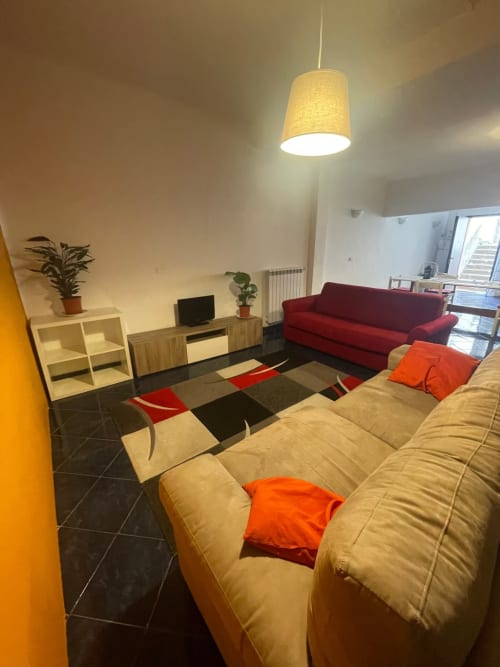 Soggiorno moderno del B&B Fossatello a Genova con divano beige, poltrona rossa, tappeto geometrico, TV e illuminazione a sospensione