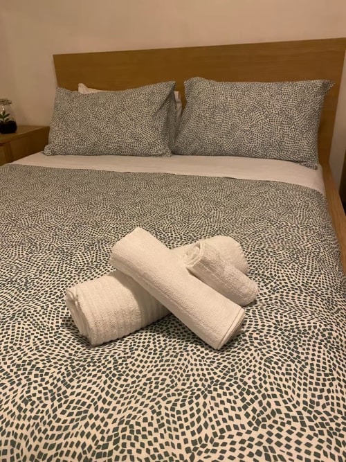 Letto con biancheria a motivi e asciugamani bianchi arrotolati presso l'appartamento B&B Fossatello a Genova