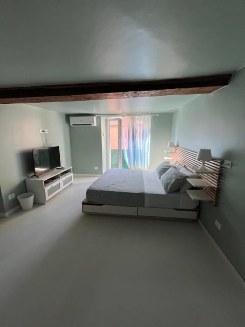Camera moderna al B&B Fossatello di Genova con letto, TV, travi in legno a vista e vista sulla città attraverso porte in vetro