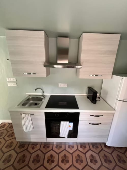 Moderna cucina in appartamento a Genova con mobili bianchi, lavello, piano cottura elettrico e cappa inox