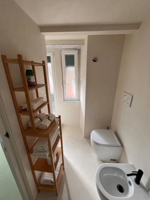 Bagno compatto con bidet e toilette, mensola in legno con asciugamani, finestra con vista sulla città a Genova B&B