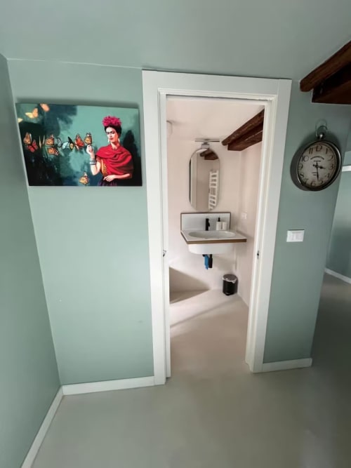 Corridoio bagno verde menta della B&B Genova con opera di Frida Kahlo, orologio vintage e lavabo moderno