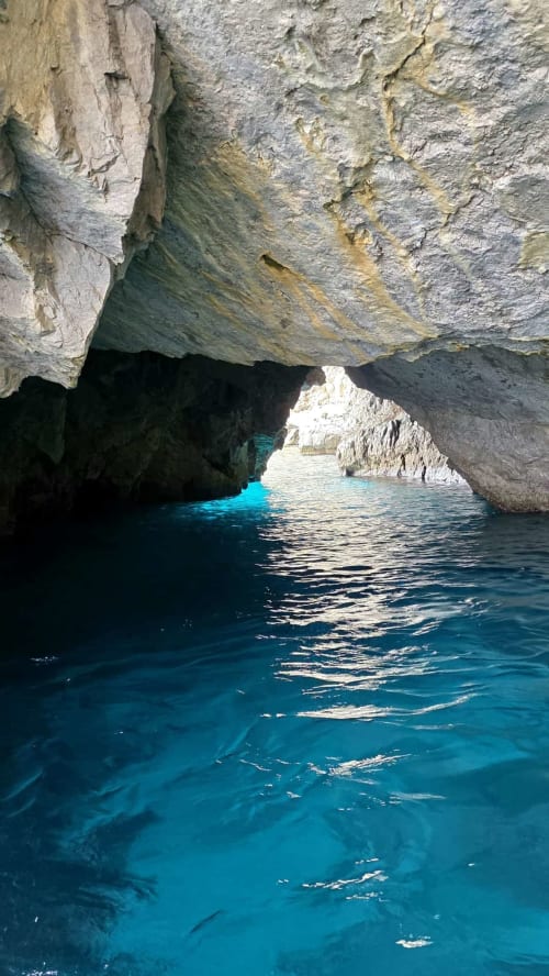 Mare turchese sotto scogliere calcaree drammatiche a Meta di Sorrento, ingresso di una grotta costiera italiana