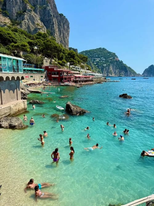 Acque turchesi della spiaggia di Meta di Sorrento con edifici a picco e bagnanti, Relais Palazzo Cacace
