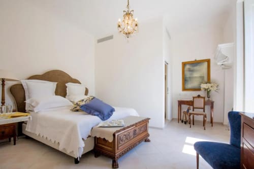 Elegante camera da letto al Relais Palazzo Cacace a Meta di Sorrento con letto in legno, biancheria bianca, lampadario di cristallo e arredamenti d'epoca
