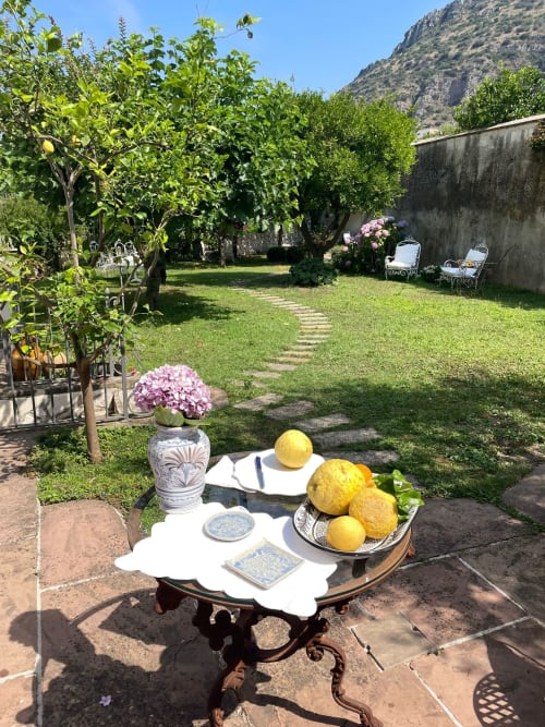 Giardino soleggiato del Relais Palazzo Cacace con limoni, piante in fiore e zona salotto con vista sulle montagne