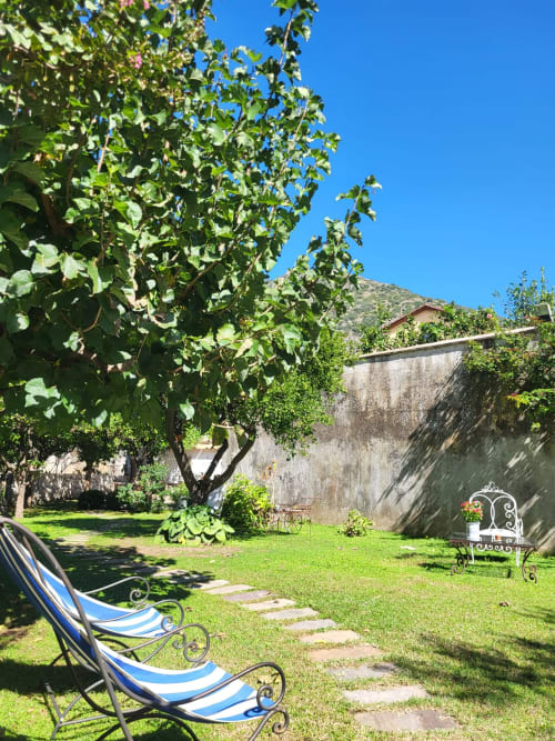 Giardino rigoglioso del Relais Palazzo Cacace a Meta di Sorrento con lettini a righe, alberi monumentali e mura della storica villa