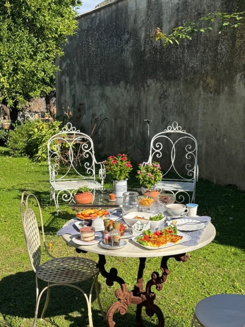 Tavolo da giardino al Relais Palazzo Cacace con eleganti sedie in ferro battuto, cibi freschi e fiori su pietra invecchiata