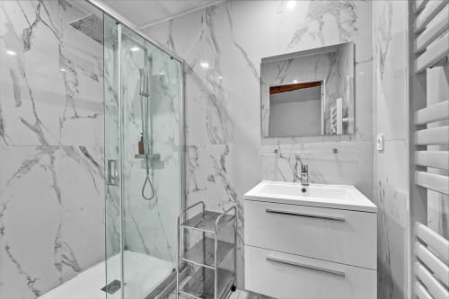 Salle de bain moderne en marbre dans un appartement toulousain avec douche vitrée, vasque blanche et porte-serviettes chauffant