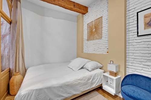 Chambre moderne aux Relais Du Capitole, Toulouse, avec mur en brique blanche, poutre apparente, lit double et fauteuil bleu