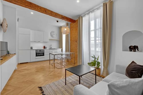 Appartement moderne ouvert à Toulouse avec cuisine blanche, salle à manger, salon avec canapé gris, parquet et vue sur la ville