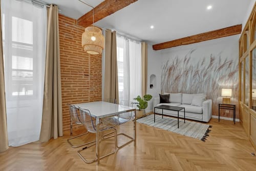 Salon moderne d'un appartement à Toulouse avec table à manger, canapé, poutres apparentes, mur en brique et vue sur la ville