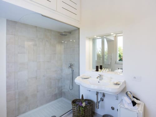 Bagno moderno con doccia in vetro, lavabo bianco a colonna e specchio presso la cottage Relais Palazzo Cacace a Meta di Sorrento