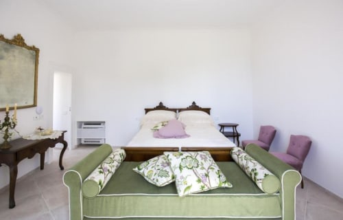 Camera elegante al Relais Palazzo Cacace a Meta di Sorrento con letto in legno, panchetta verde e vista sul giardino