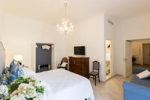 Spaziosa camera da letto al Relais Palazzo Cacace a Meta di Sorrento con elegante lampadario, cassettiera in legno, TV e accenti blu