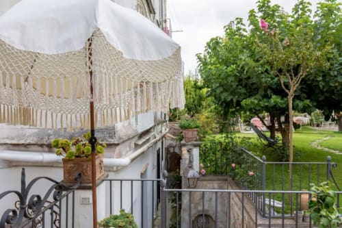 Terrazza della cottage Relais Palazzo Cacace con baldacchino in macramé, vista sul giardino, piante fiorite e rigogliosa vegetazione a Meta di