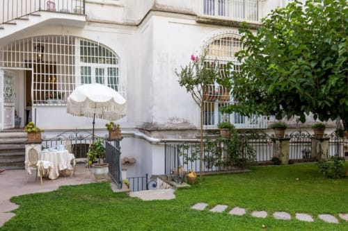 Elegante corte giardino del Relais Palazzo Cacace a Meta di Sorrento con ombrellone bianco, zona relax e lussureggiante vegetazione