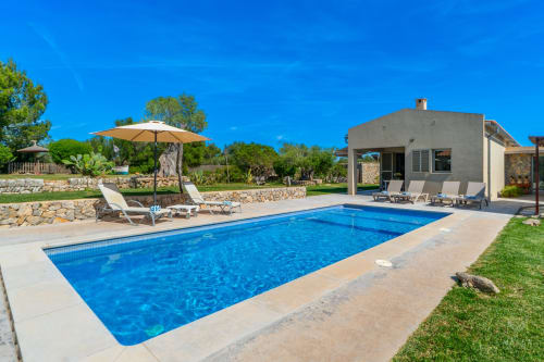 Villa de lujo en Artà con piscina rectangular, tumbonas, sombrillas y casa moderna con vistas al Mediterráneo