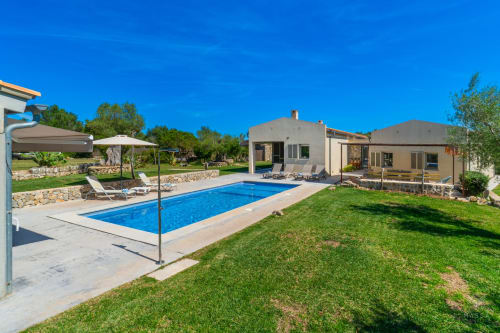 Villa de lujo en Artà con piscina rectangular, tumbonas, jardín cuidado y construcciones de piedra modernas bajo cielo azul despejado