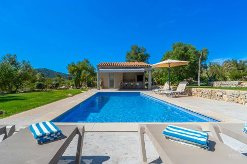 Villa de lujo con piscina en Artà, agua azul, tumbonas, terraza de piedra y jardines mediterráneos bajo cielo despejado
