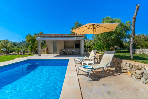 Villa de lujo con piscina en Artà, cabaña moderna en la zona de piscina, sombrilla amarilla, tumbonas y jardines bajo cielo azul