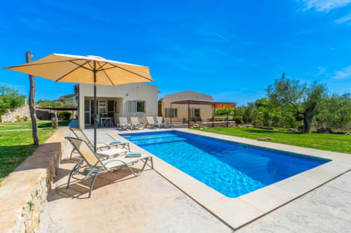 Villa en Artà con piscina rectangular, tumbonas, sombrilla amarilla y terraza de piedra con vistas a exuberantes jardines