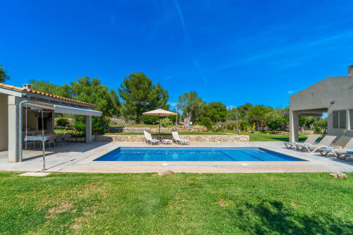 Villa de lujo en Artà con piscina azul, tumbonas, terrazas de piedra y jardines mediterráneos bajo cielo despejado