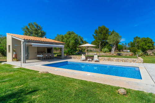 Casa de piscina moderna en Artà con piscina rectangular azul, terraza, tumbonas y jardín mediterráneo bajo cielo despejado