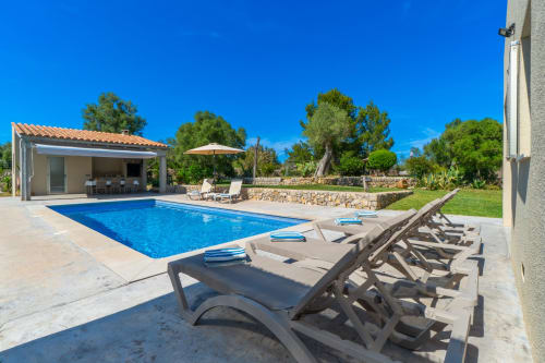 Lujosa área de piscina en Massa Properties en Artà con tumbonas, arquitectura mediterránea y exuberantes jardines bajo cielo azul despejado