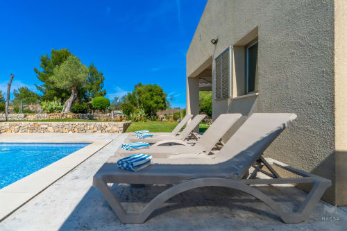 Tumbonas de lujo frente a la piscina en Massa Properties de Artà con aguas azules del Mediterráneo y arquitectura moderna